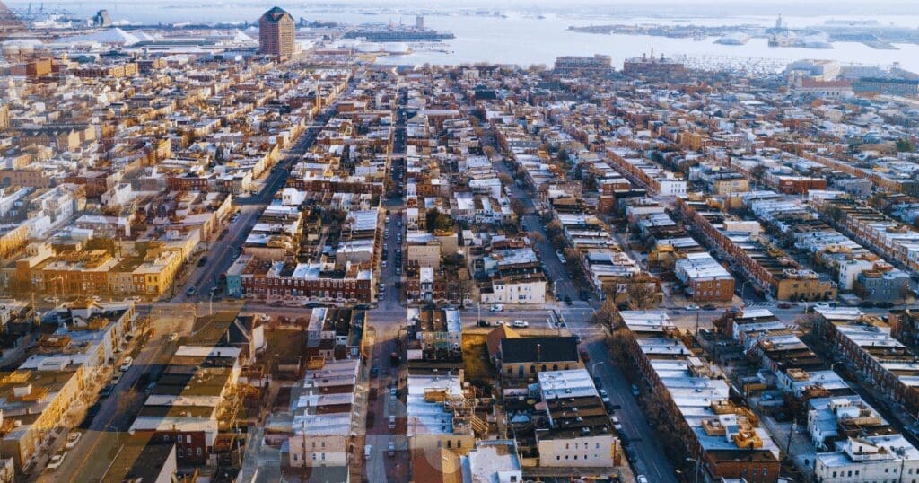 A sweeping aerial view of tightly packed historic brick rowhomes in downtown Baltimore City. Because these unique urban properties share vertical structural masonry walls, a single neighbor suffering from flat roof ponding water can easily cause lateral moisture to migrate straight through the parapet brick and completely destroy adjoining plaster interiors.